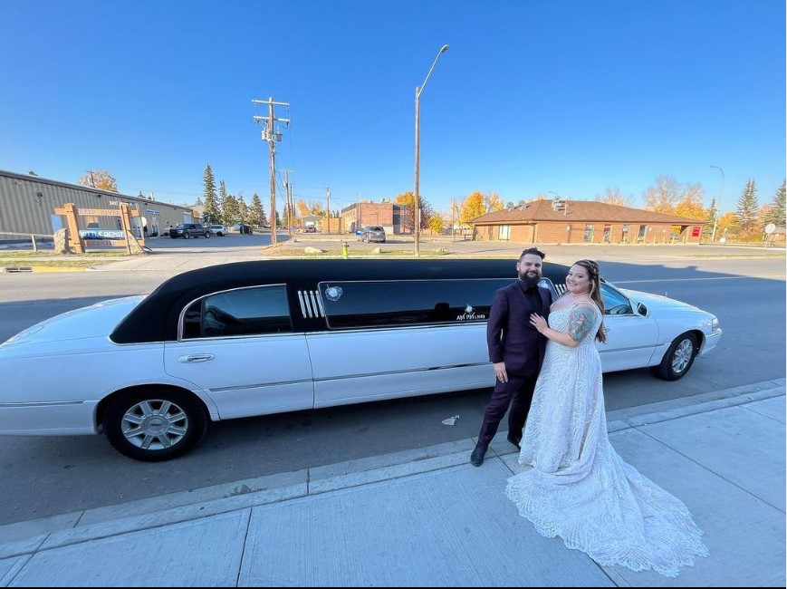 Bride and groom posing in front of a white limousine.