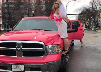Bride to be standing on the running board of a pink Dodge Ram Limo, wearing a white dress with a pink sash