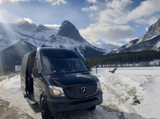 Mercedes Mini Black Party Bus parked in Canmore in front of snowy Rocky Mountains