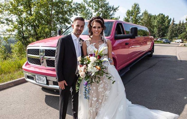 Beautiful bride and Groom pose for photo in front of pink Dodge Ram Limo