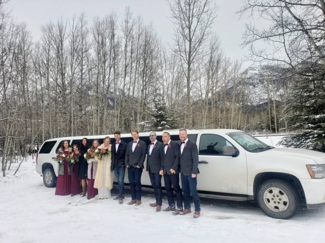 Winter wedding Party photo in front of white Suburban Limousine