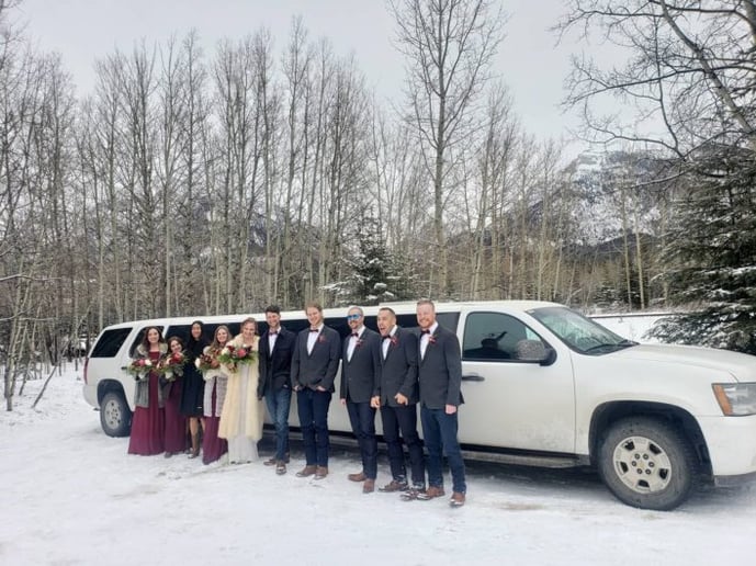 Winter Wedding Party pose for photo in front of White Suburban Stretch Limousine