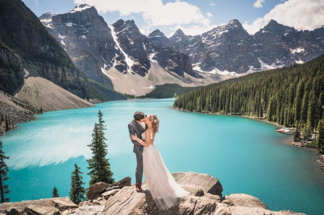 Bride and groom kiss in front of Moraine Lake with Rocky Mountains in background