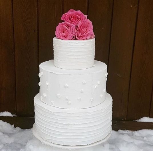 White 3 tier wedding cake with 3 pink flowers on top