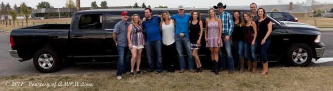 Group of adults with cowboy hats celebrating in front of black Dodge Ram limousine