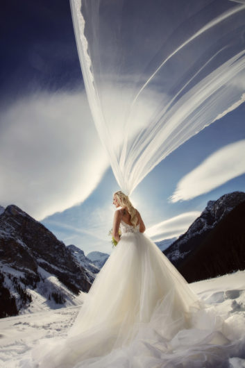 Bride in white gown standing on top of snowy mountain