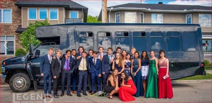 Group dressed up for prom taking photo in front of black party bus