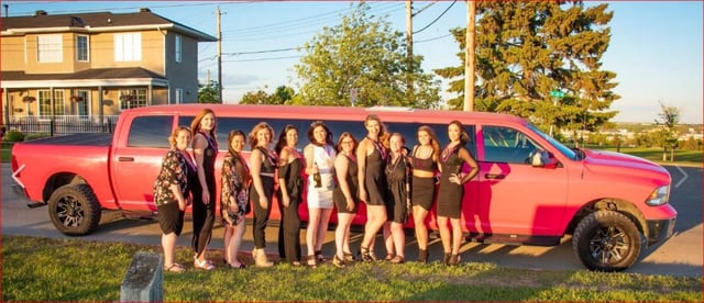 10 ladies in black and one in white celebrating stagette in front of pink Dodge Ram Limousine