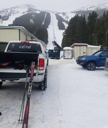 Truck bed of white Dodge Ram Limousine, filled with skis and ski hill in background