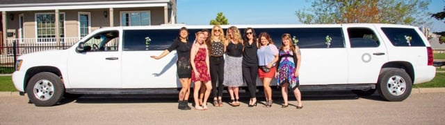 Group of 7 people pose for photo in front of white Suburban Stretch Limousine