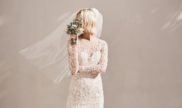 Bride in white wedding gown, holding bouquet in front of her face