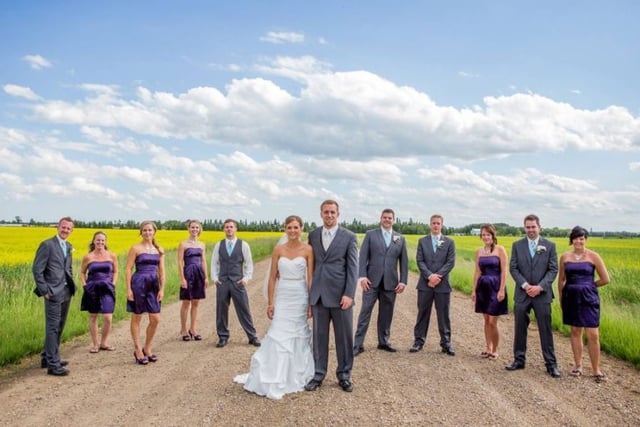 Wedding party standing in field with blue sky and clouds behind them