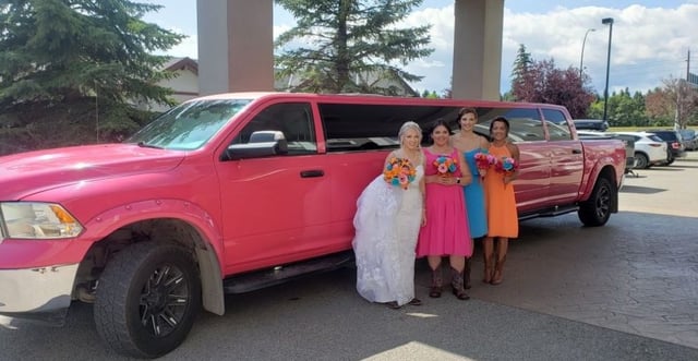 Bride and 3 bridesmaids standing in front of pink Dodge Ram Limo on wedding day