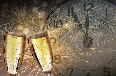 2 glasses of champagne in front of clock that is 5 minutes to midnight onNew Year's Eve