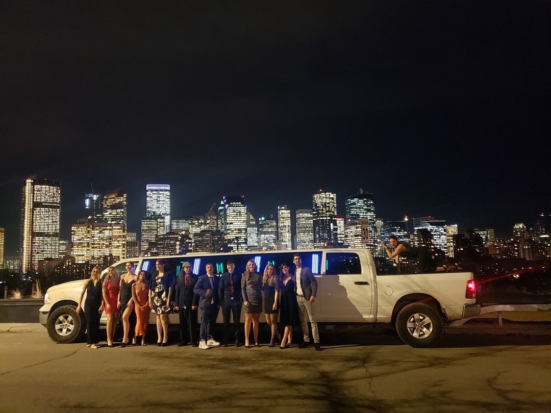 Group photo in front of white Dodge Ram Limousine and city of Calgary skyline at night