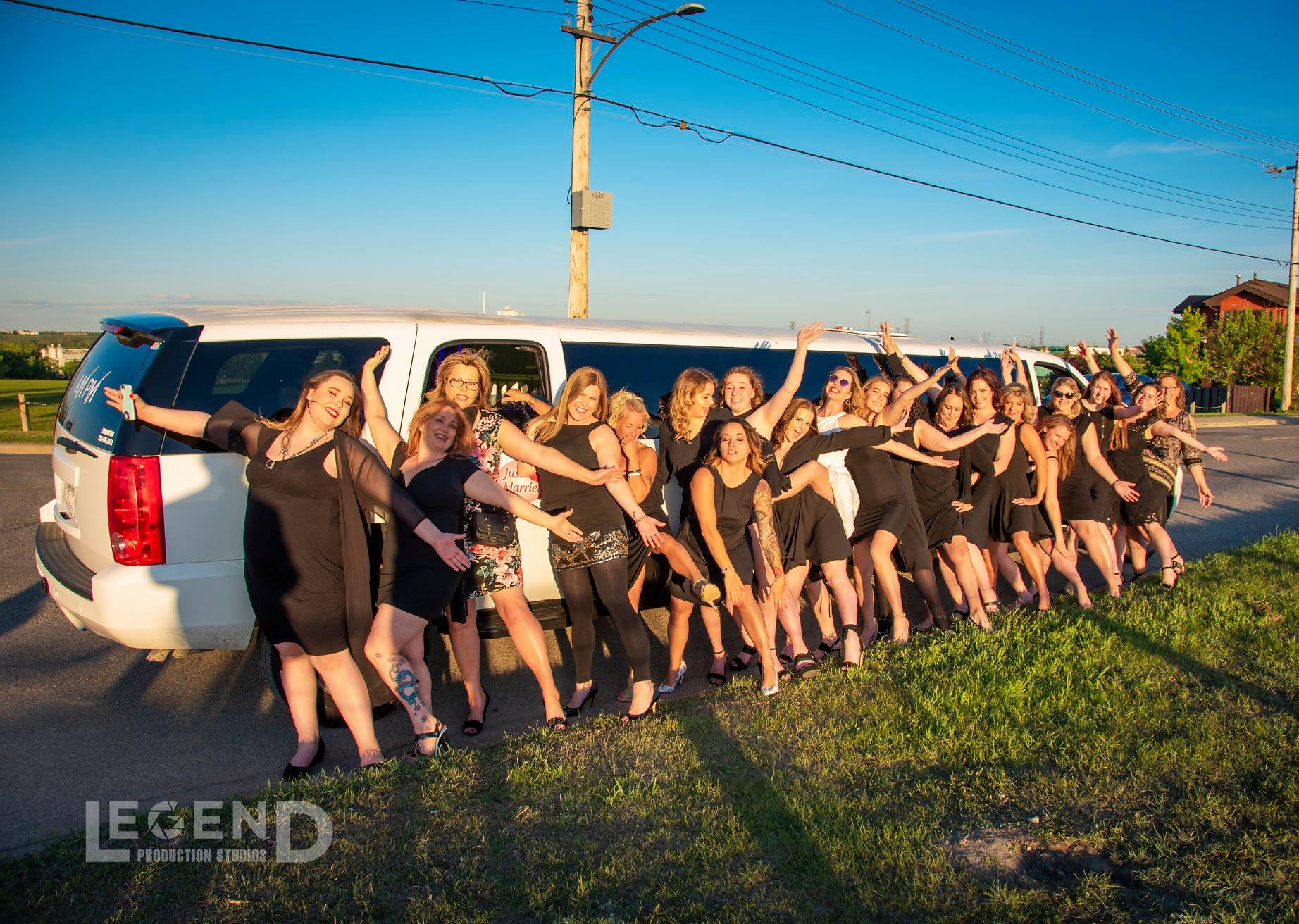 Group of ladies in black dresses posing in front of a WhiteSuburban Limo