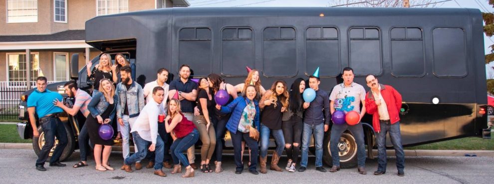 Group posing for silly photo in front of black party bus at birthday celebration